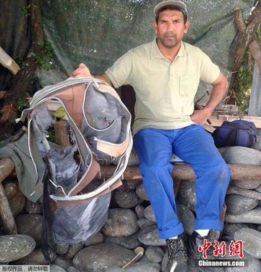 圖為當(dāng)?shù)貢r間7月30日，留尼旺島上的一名海岸清潔人員展示他找到的一個手提箱的殘骸。